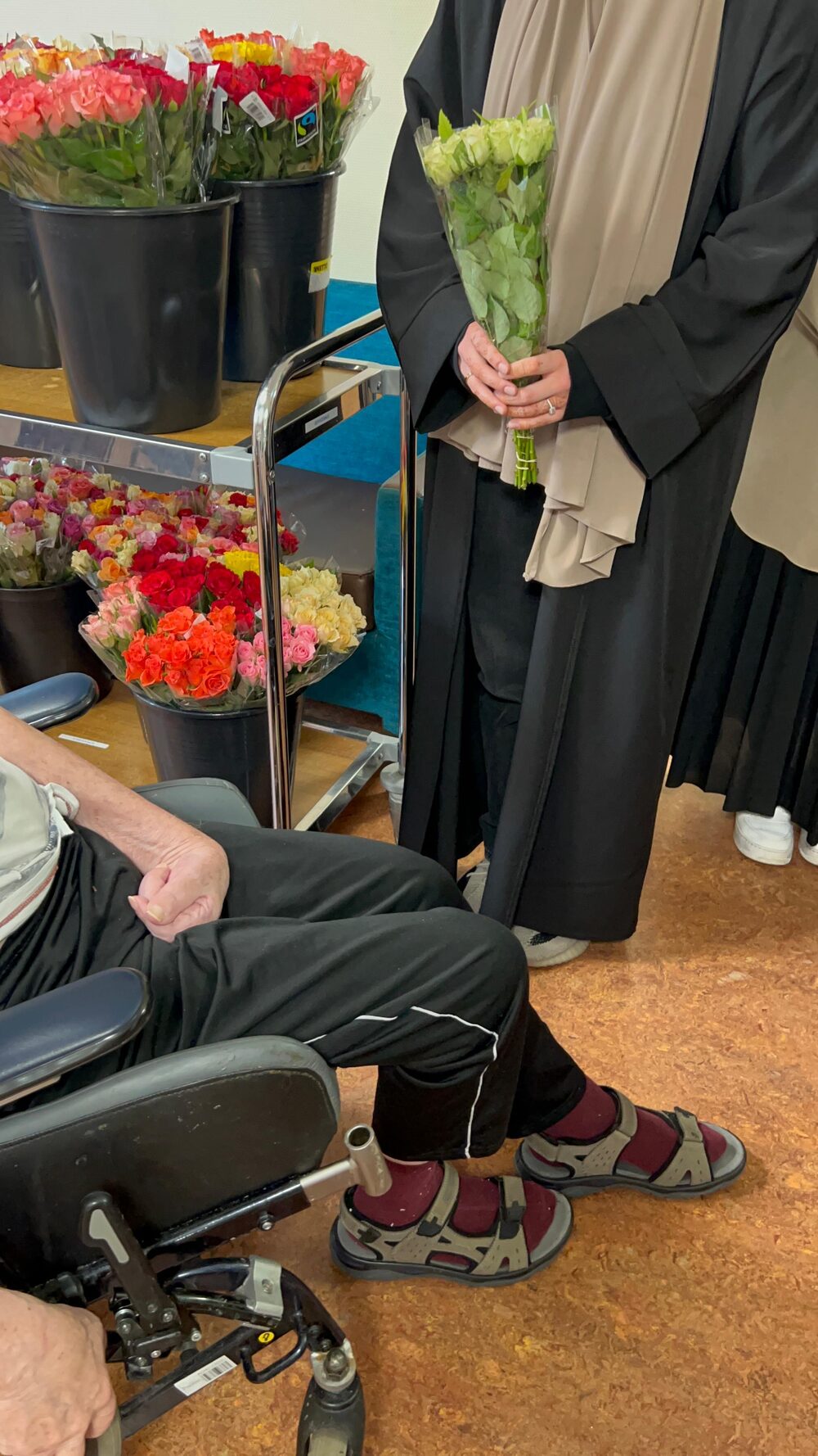 Een vrijwilliger met een bos witte rozen naast emmers vol bloemen in het woonzorgcentrum